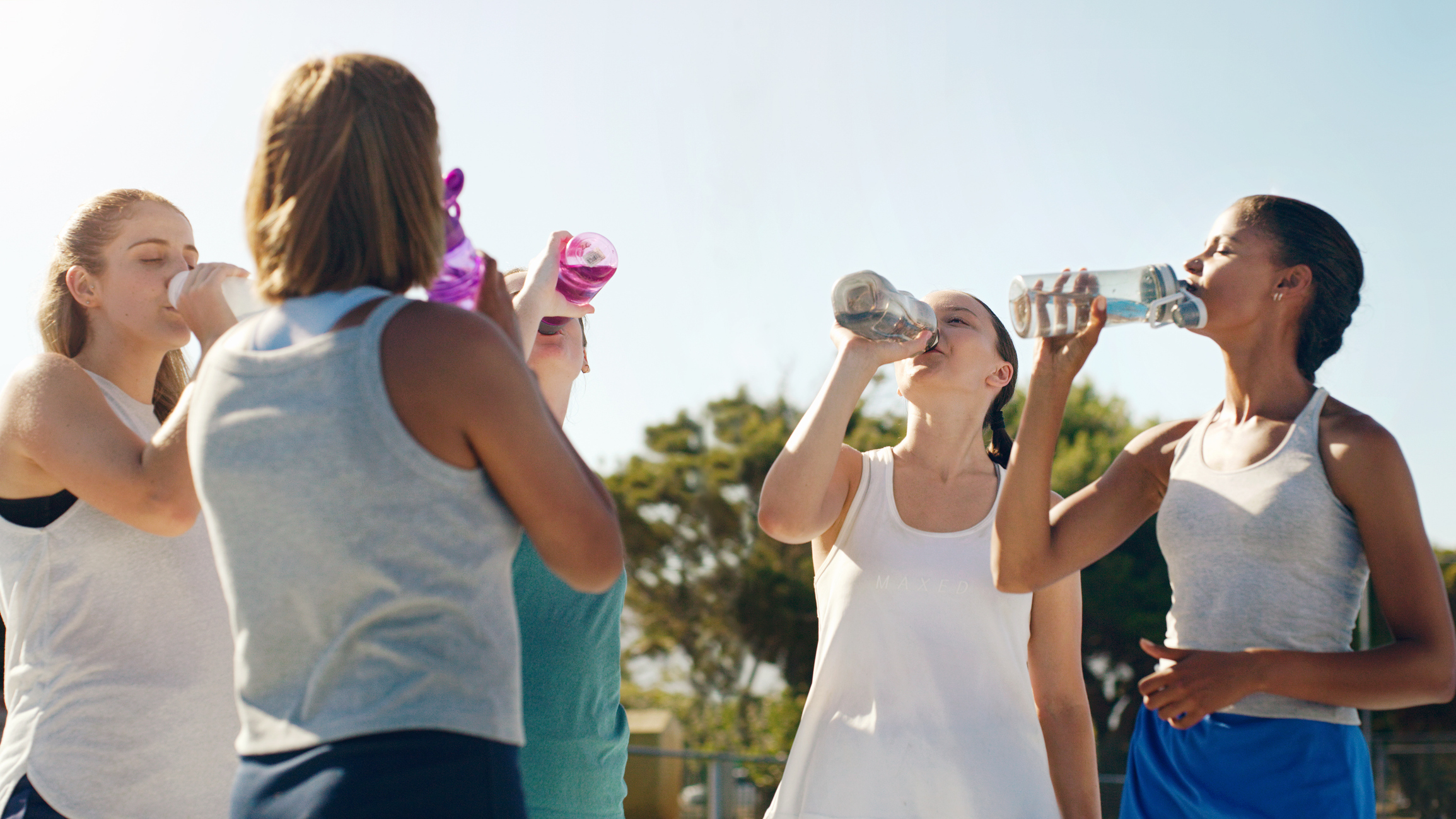 Athletic woman, friends and drinking water for hydration during sports workout, training or practice together outside